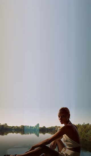 Bilde av en modell som har på seg en av Winter Sun-kapselinnsamlingsstykkene som sitter foran en vakker innsjø