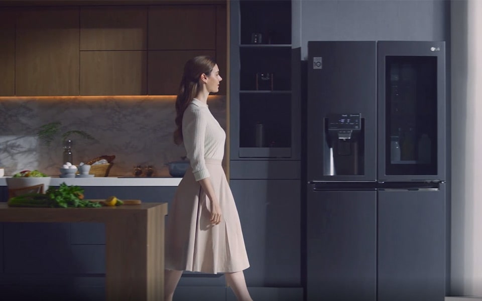 A woman walking up to a LG Instaview Door-In-Door Refrigerator