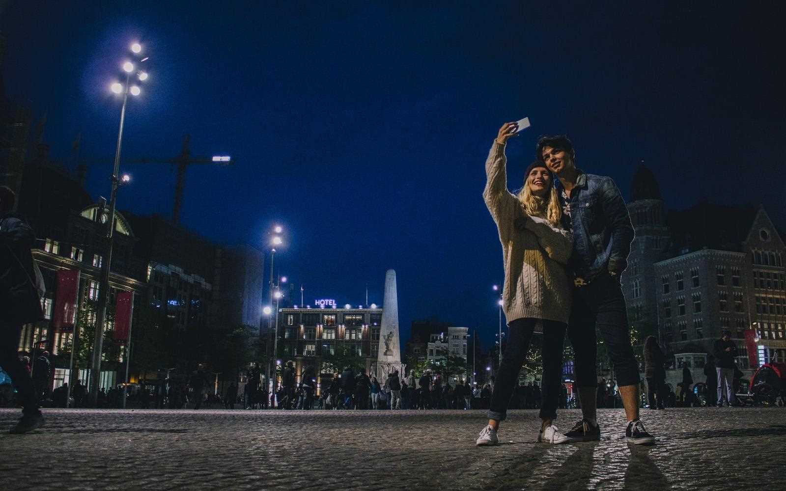 Uśmiechnięta para robi selfie smartfonem LG K40 nocą na tle krajobrazu miasta