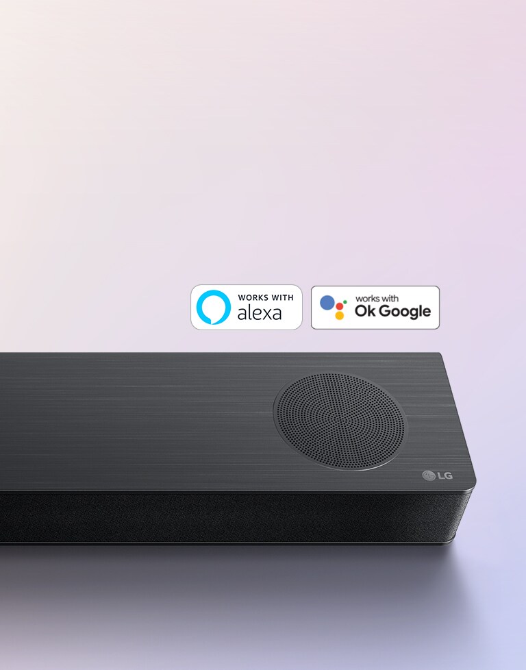 LG Soundbar står på marken och LG:s logotyp är synlig i soundbarens högra hörn. Logotyperna för Alexa och OK GOOGLE är synliga på soundbaren.