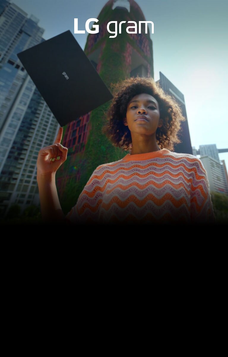 a woman with LG gram laptop on her finger looking down, buildings behind her